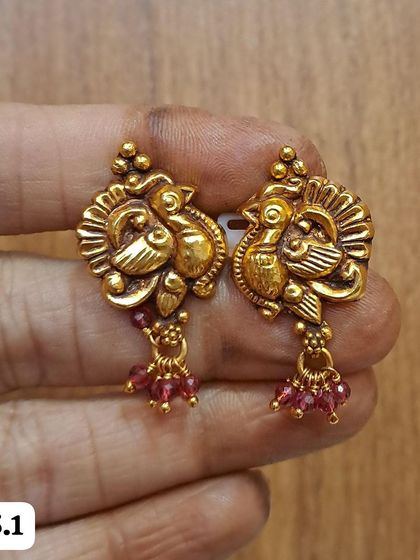 These peacock motif earrings are made from antique-finished 92.5 silver and have ruby-colored bead drops. They are perfect for adding a small pop of color.