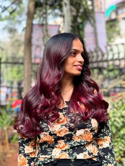 A smiling client enjoying her new wine red hair. The color is bold, confident, and full of life.