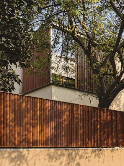This building uses vertical wooden slats for both the facade and the boundary fence. This creates a unified architectural language and acts as a continuous screen that filters light and views, providing privacy from the street.