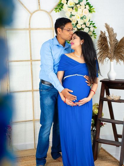 A tender moment captured in our studio. The partner places a gentle kiss on the mom-to-be's forehead as they both hold the baby bump, dressed in coordinating blue outfits.