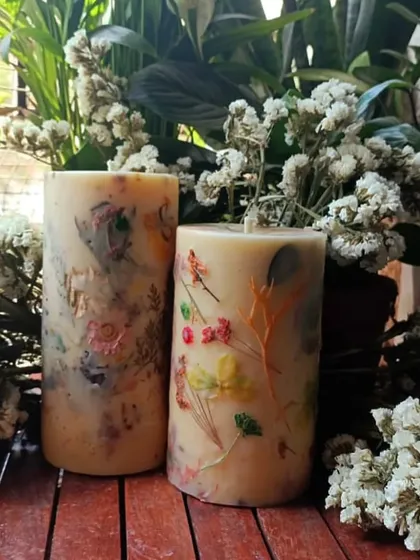 Two of our floral love pillar candles, standing tall amidst a bed of dried flowers. They are perfect as wedding gifts, housewarming presents, or simply to add a touch of luxury to your home.