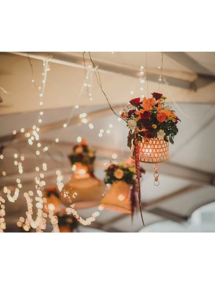 Hanging wicker lamps adorned with flowers, part of the decor for an outdoor balcony space at a reception, creating a warm and rustic ambiance.