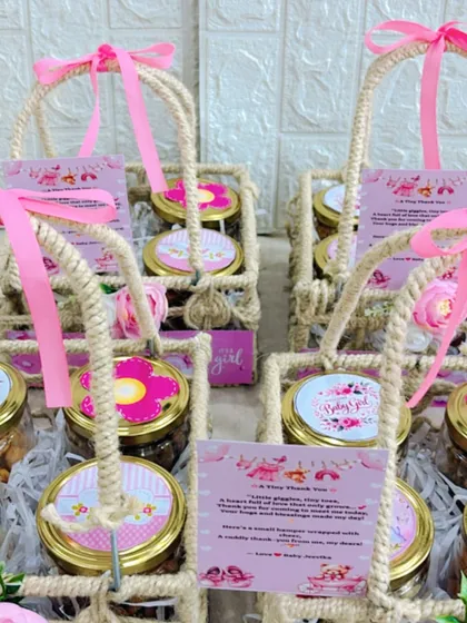 An array of "It's a girl" announcement favors in jute baskets, each tied with a pink ribbon and featuring a personalized thank you card.