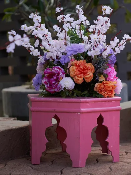 A beautiful floral arrangement in shades of pink, purple, and orange, placed on a decorative pink stool. These small touches of color brighten up any corner.
