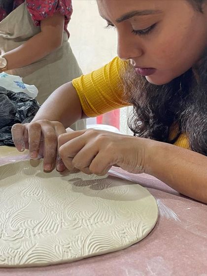 A student impresses a texture mat onto a clay slab to create an intricate pattern for a plate.