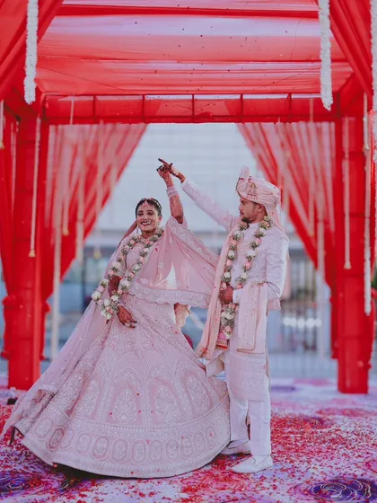 A beautiful wide shot of the couple dancing under a vibrant red mandap, with flower petals scattered on the floor.