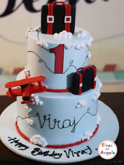 The cake is a centerpiece of any celebration. This custom two-tier cake was designed for a 'Travel Theme' first birthday, featuring edible airplanes, suitcases, and clouds to celebrate Viraj's first trip around the sun.