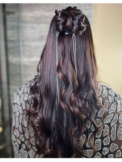 A chic and modern party hairstyle. This look features a half-up bun with long, flowing curls, accented with delicate silver hair chains for a touch of sparkle.