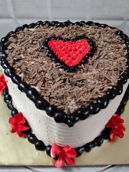 A heart-shaped black forest cake. The top is covered with chocolate shavings and a piped red heart in the center.