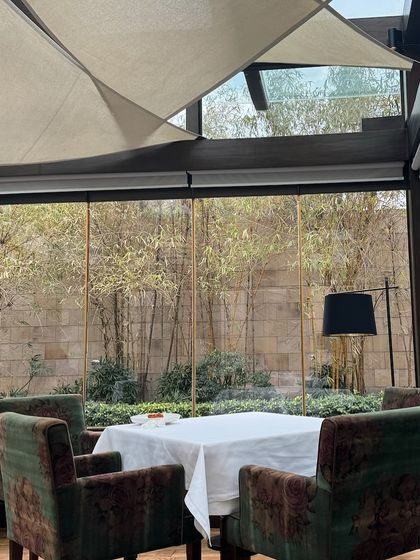A quiet table framed by glass and grounded by wood, overlooking a serene bamboo garden. This is a sanctuary where you can escape the city and immerse yourself in the meal.