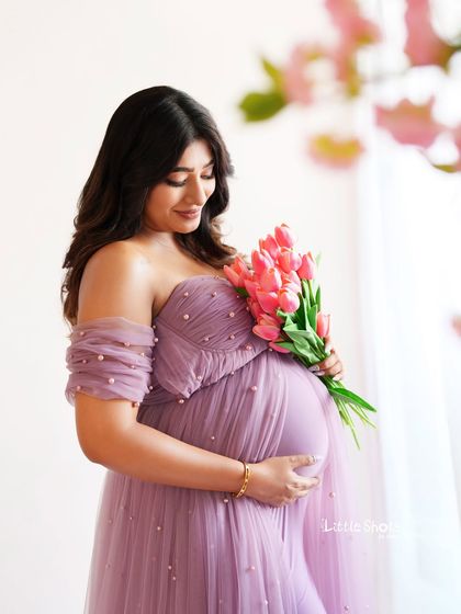 A serene portrait of a mother-to-be holding a bouquet of pink tulips. She is wearing a beautiful pearl-studded lavender gown, her expression soft and peaceful.