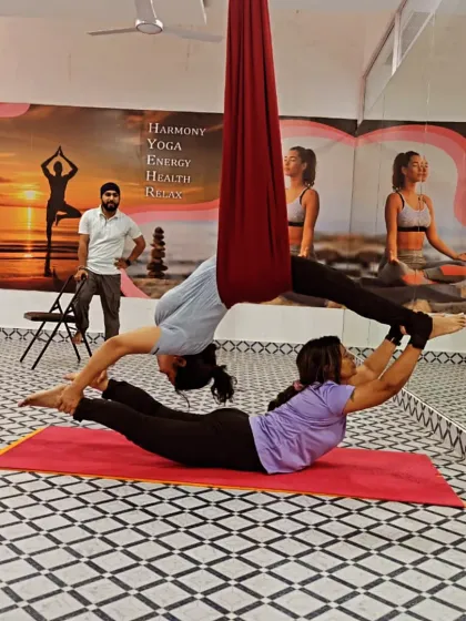 Two students work together in a partner pose, with one using the aerial hammock for support. This demonstrates how we blend different yoga styles in our studio.
