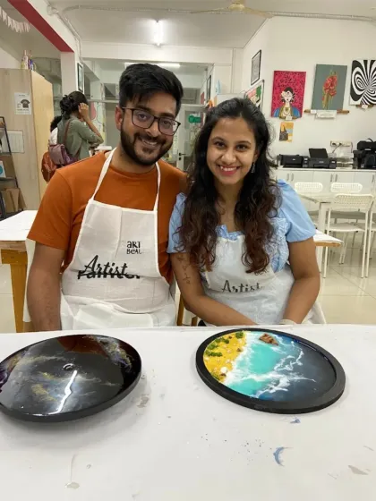A couple showcasing their resin art. One piece is a galaxy design, and the other is a beach scene, highlighting the different themes available in my resin workshops.