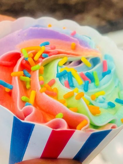 A close-up shot of a single rainbow cupcake in a striped paper liner. You can see the detail in the multi-colored frosting swirl.