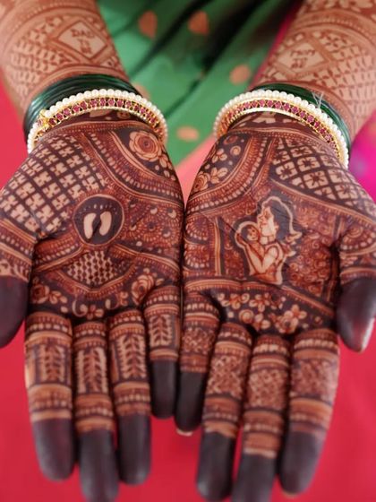 A beautiful baby shower mehendi with a rich, dark stain. The design includes a portrait of a mother holding her baby and tiny baby footprints on the other palm.