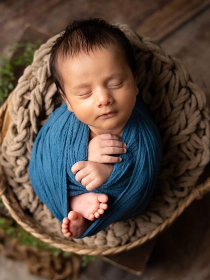 A classic potato sack pose, where the baby is wrapped snugly to feel secure and sleepy. The deep blue wrap provides a beautiful pop of color against the rustic backdrop.