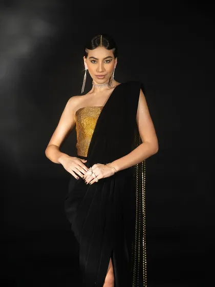 A medium shot from the Nikhil Thampi lookbook. The model's pose is directed to feature the gold bustier and the drape of the black fabric, providing a clear view of the design.