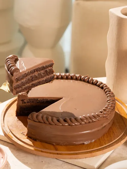 The perfect slice being lifted from a classic, glossy chocolate cake. This shot is all about the clean lines and the promise of a rich, moist dessert.