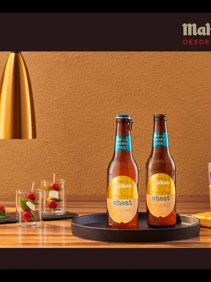 A social setting featuring two Mahou Wheat bottles and a poured glass. The warm, focused lighting creates an intimate mood, perfect for depicting a shared experience.