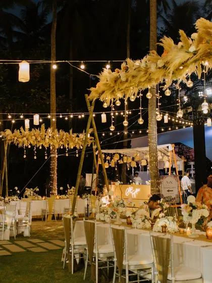 The dining setup for the seaside soirée, with long tables under a canopy of pampas grass and hanging glass orbs, creating an intimate and enchanting atmosphere.