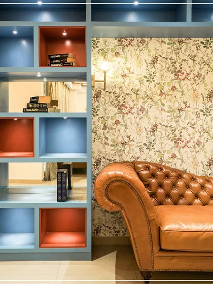 A cozy reading corner with a tan leather Chesterfield sofa next to a custom blue and red bookshelf, showcasing a playful use of color.