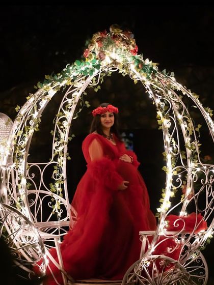A true fairytale moment. This outdoor night shot features the mom-to-be in a red gown, seated in a beautifully lit Cinderella carriage, creating a magical and unforgettable image.