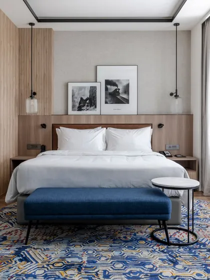 A guest room at Radisson Resort, Khopoli, designed as a tranquil retreat. The space features a clean material palette, a comfortable king-sized bed with a custom headboard, and curated black-and-white artwork that reflects the local landscape, balancing modern aesthetics with guest comfort.