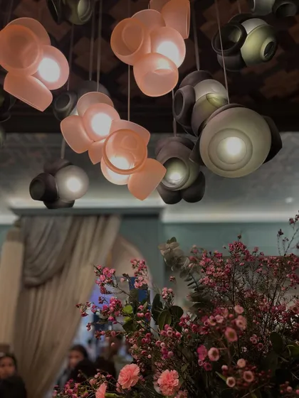 A close-up of the Bocci 100 series pendants, with soft pink flowers in the foreground, highlighting the fixture's delicate colors and organic shapes.