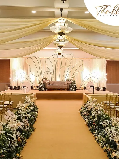 An elegant reception stage with a backdrop of draped fabric and a custom shell-like design. The aisle is lined with beautiful white floral arrangements, creating a sophisticated and dreamy path.
