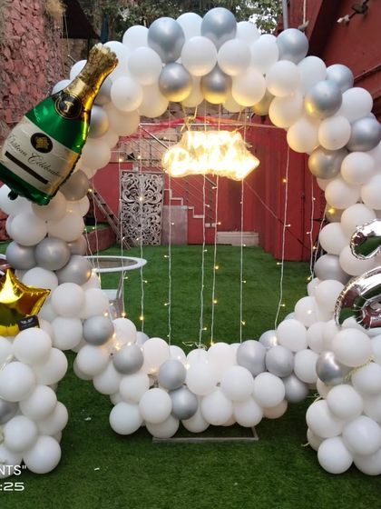 A circular balloon arch in white and silver for a 23rd birthday celebration, set up outdoors on an artificial lawn for a fresh, modern look.
