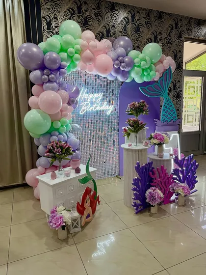A glamorous mermaid theme with a sequin backdrop, neon sign, and a pastel balloon arch. The mermaid tail and Ariel cutout complete this stylish setup.