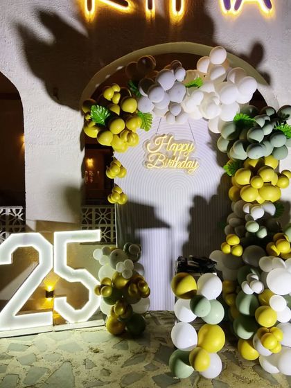 A close-up of a stylish outdoor decoration for a 25th birthday. This setup includes an arched backdrop and an organic balloon garland in a sophisticated palette of sage green, gold, and white.