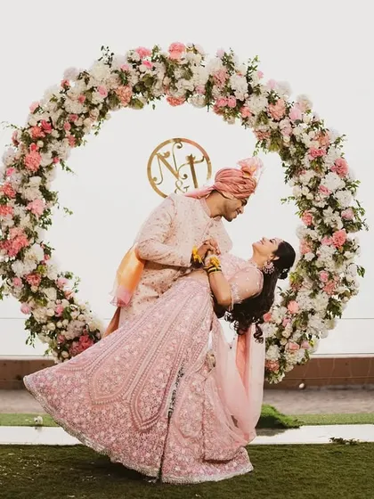 A fun and romantic dance pose in front of a circular floral arch. The bride's lehenga twirls beautifully, adding a sense of movement and joy to this stunning portrait.