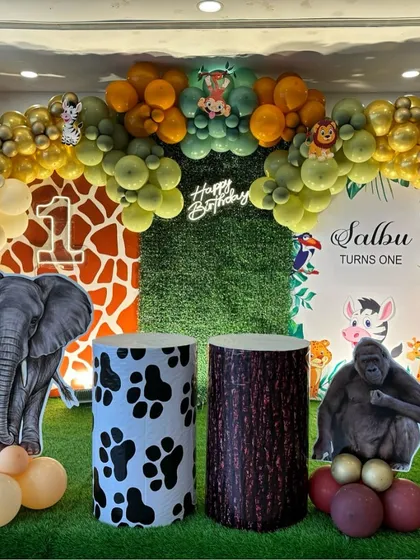 An immersive jungle theme birthday decoration. This setup features a lush green grass backdrop, animal cutouts of an elephant and gorilla, and an organic balloon arch in shades of green, orange, and gold to create a wild safari atmosphere.