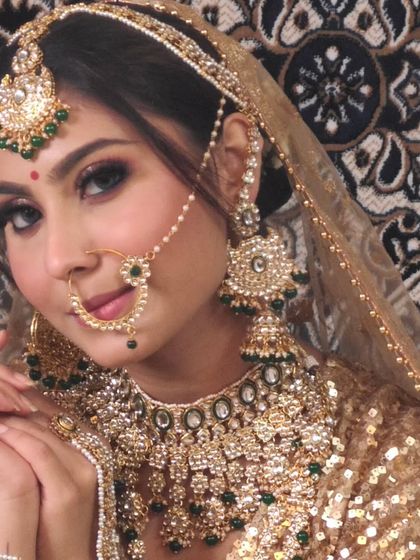 A close-up of a bride in a gold sequin lehenga, complemented by a heavy Kundan and green bead jewellery set. The jhumkas and nath are beautifully detailed.