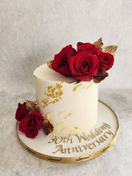A simple and classic anniversary cake. The white buttercream is decorated with fresh red roses and a touch of gold leaf for an elegant finish.