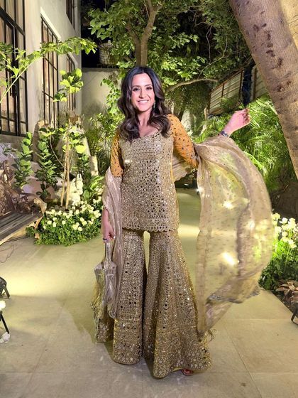 A client looking radiant in a heavily embellished sharara suit. Her hair is styled in glamorous waves, and the makeup is kept luminous to complement the sparkling outfit.