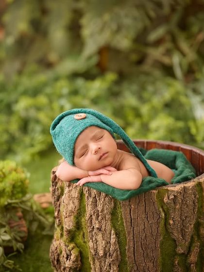 This newborn, dressed as a little woodland elf, sleeps peacefully inside a prop designed to look like a real tree stump, surrounded by greenery.
