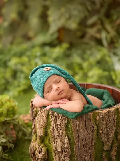 This newborn, dressed as a little woodland elf, sleeps peacefully inside a prop designed to look like a real tree stump, surrounded by greenery.