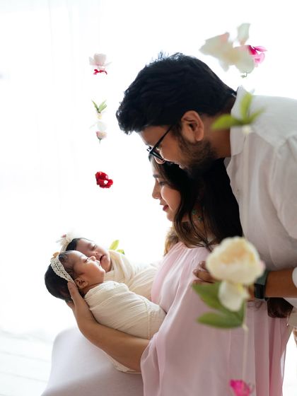 It was raining twins in the studio! A beautiful family portrait with mom and dad admiring their two newborn twin girls, framed by delicate hanging flowers.
