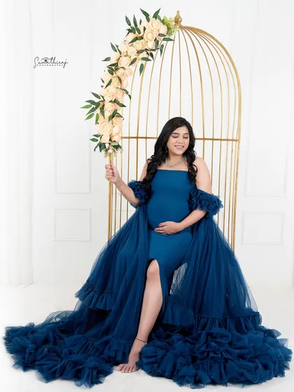 A stunning portrait of a mother-to-be in a royal blue gown, seated in a golden birdcage prop. The floral accents and elegant styling create a truly magical and unique image.