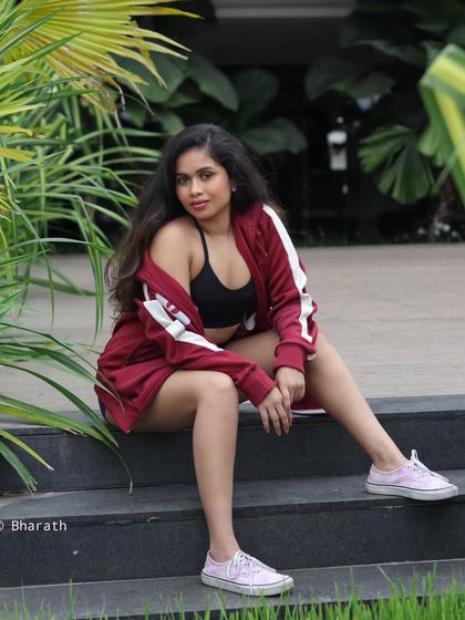 A relaxed, seated pose in a modern outdoor setting. The combination of athleisure wear and natural greenery creates a fresh, energetic vibe.