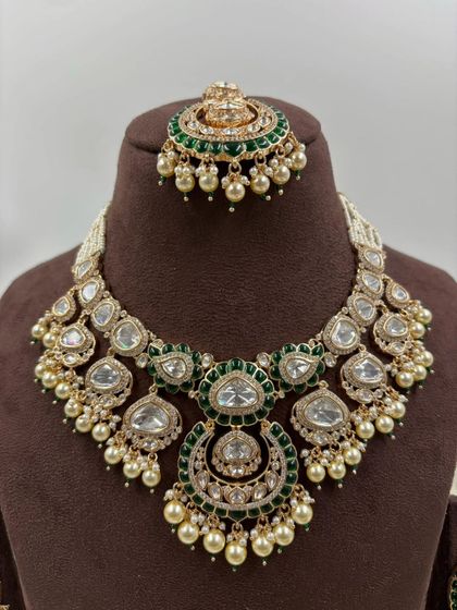 One of our most requested bridal sets, this design features large uncut Kundan stones, green Meenakari work, and pearl detailing. The set includes a necklace, chandbali earrings, and a matching maang tikka.