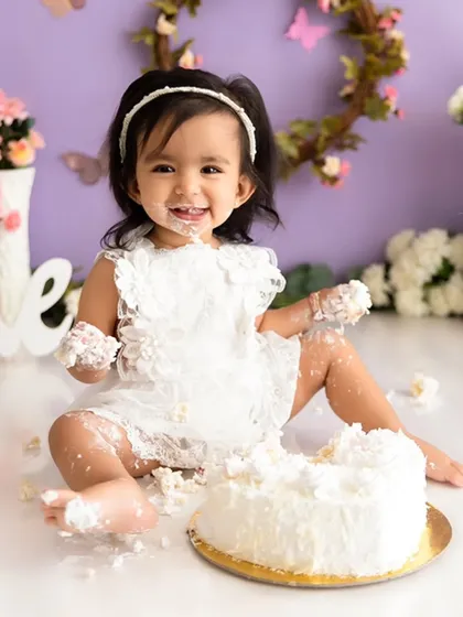 A happy moment from a butterfly-themed cake smash, showing a baby girl with a delightful, frosting-covered smile.