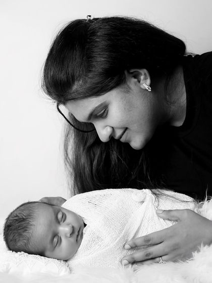 A tender black and white moment between a mother and her sleeping newborn. The soft lighting and her gentle gaze create a peaceful and loving atmosphere.