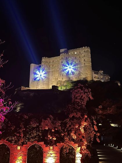 The magnificent Alila Fort Bishangarh lit up at night. The projection mapping on the fort walls adds a modern, magical touch to this historic venue, perfect for a grand wedding reception.
