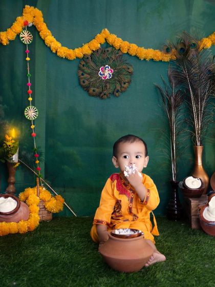 A creative take on a cake smash with a 'Little Krishna' theme. Here, the baby enjoys a pot of 'makhan' (curd) in a beautifully decorated festive setting with marigold flowers and peacock feathers.
