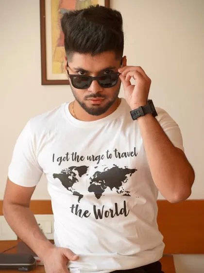 A confident portrait where the model adjusts his sunglasses. This action shot adds a dynamic and cool element to a simple t-shirt look.