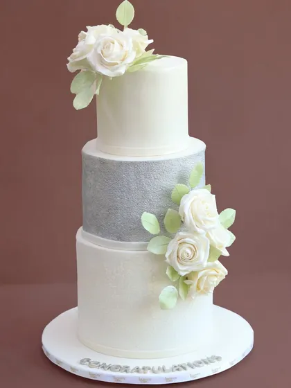For a truly timeless celebration, this white and silver tiered cake combines classic elegance with modern texture. Each sugar flower is handcrafted petal by petal, creating a sophisticated look for a wedding or grand milestone.