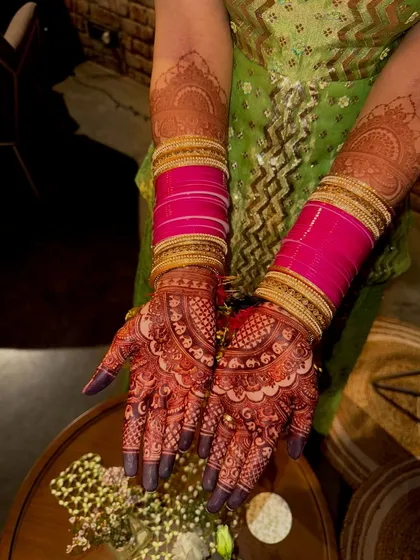 A beautiful shot of a bride's hands, adorned with pink bangles that complement the deep red of her mehendi stain.